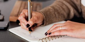 crop woman writing down notes in diary